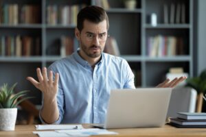 Man with confused look sat down at laptop table